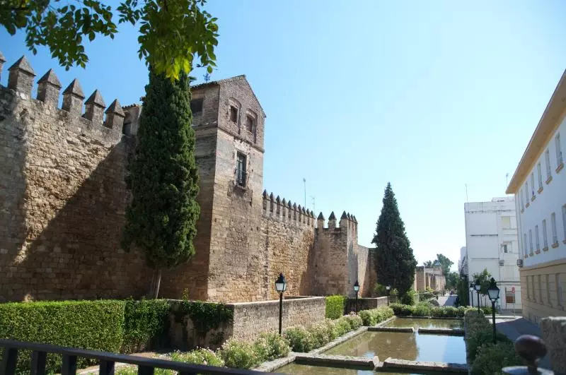 Historische Mauer und Turm mit Zypressen an einem Wasserbecken in Andalusien