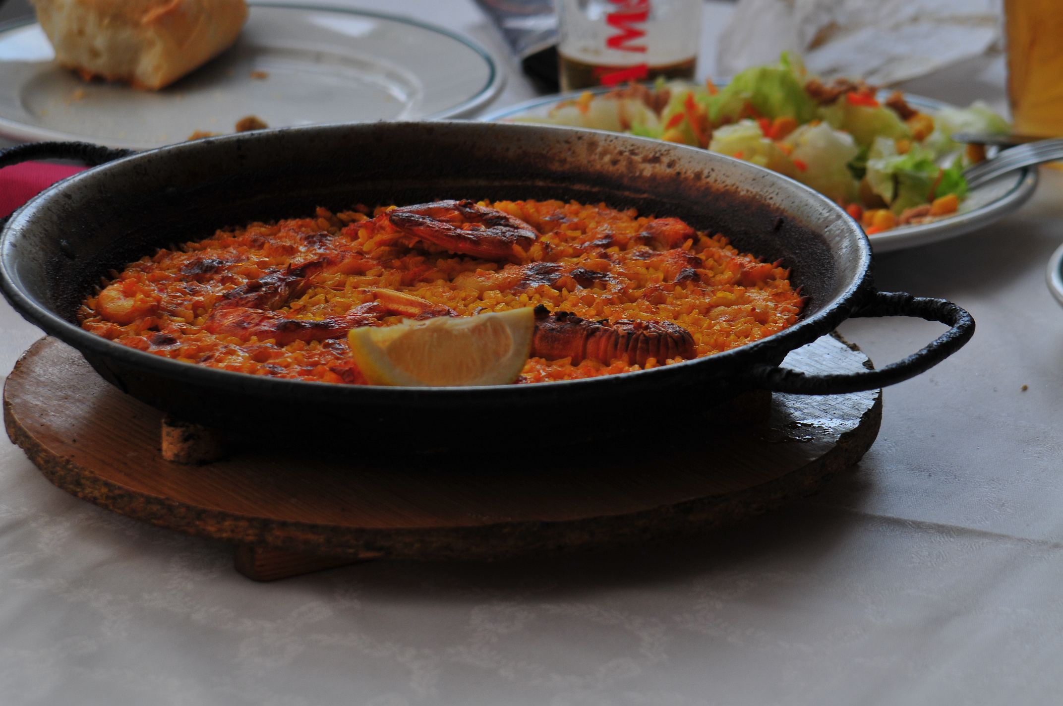Paella in einer schwarzen Pfanne mit Garnelen, Zitronenspalte und Beilagensalat. Paella in einer schwarzen Pfanne mit Garnelen, Zitronenspalte und Beilagensalat.