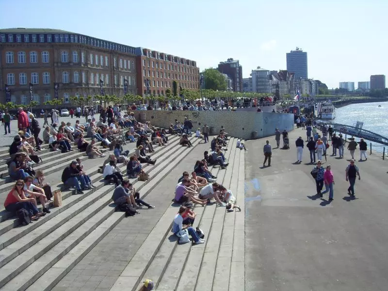 Menschen sitzen auf breiten Treppen an der Rheinpromenade in Düsseldorf